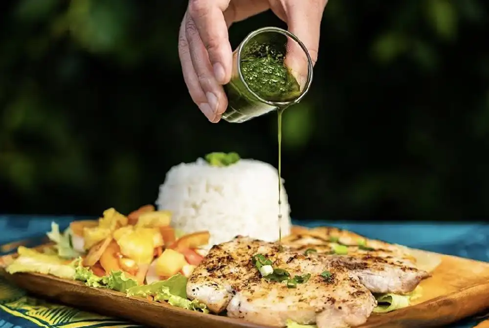 Une personne verse de la sauce sur un plat de poisson grillé du lagon de Moorea sur une table de restaurant