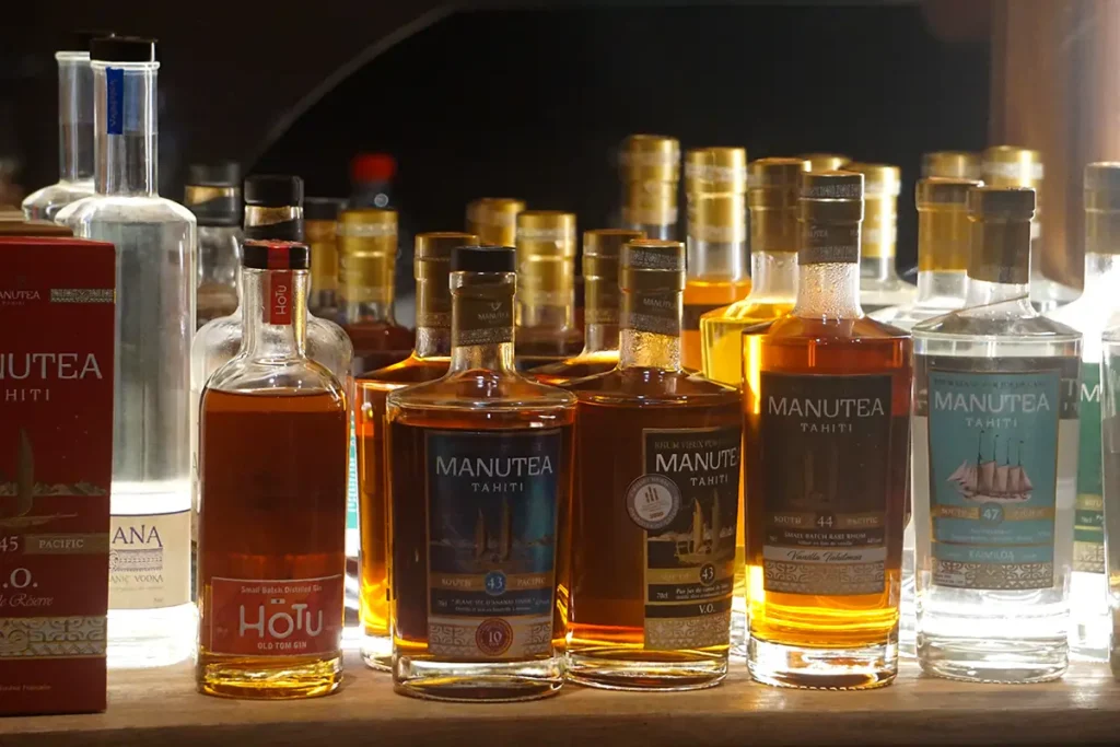 Des bouteilles de rhum Manutea Tahiti sont posées sur une étagère en bois avec un éclairage mettant en valeurs les couleurs ambrées du rhum