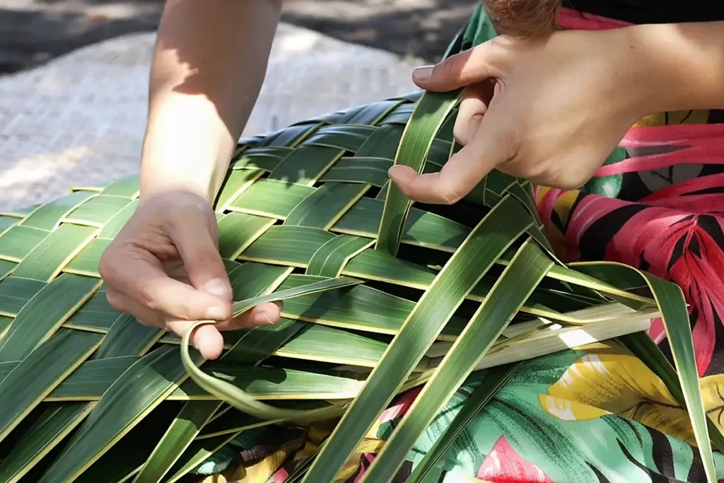 Gros plan sur les mains d'une femme tahitienne qui tresse une palme de cocotier en Polynésie.