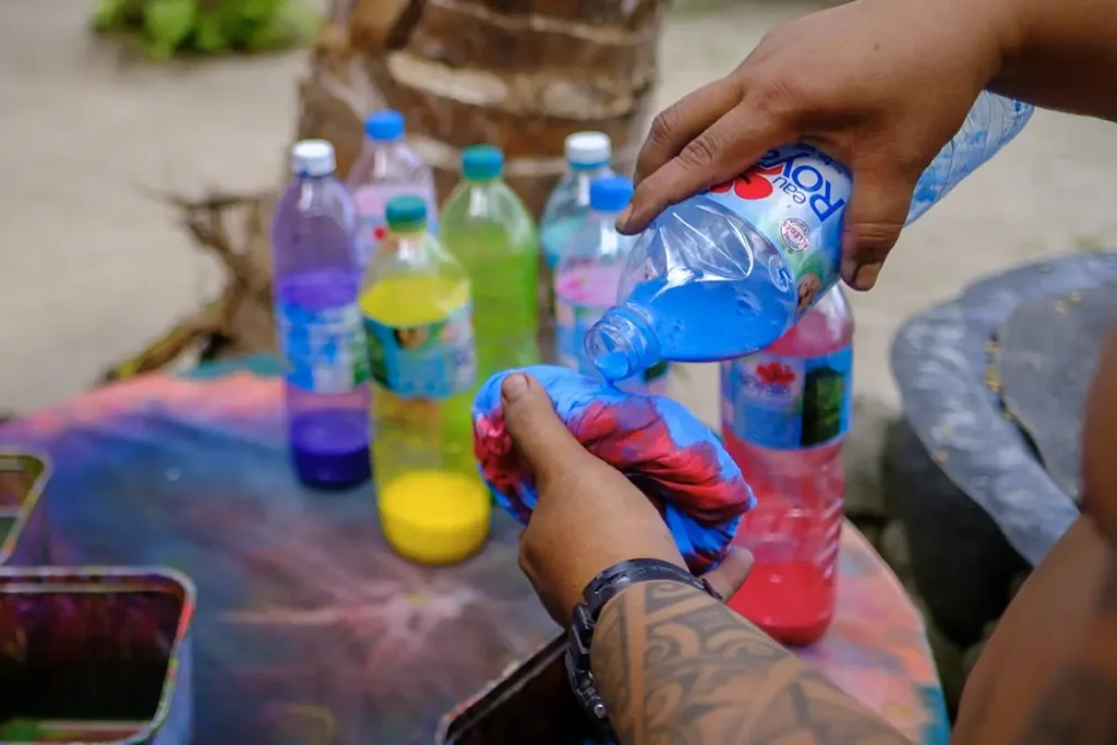 Gros plan sur les mains d'un homme tahitien qui vers de la teinture de couleur sur un tissus de paréo lors d'un atelier culturel en Polynésie