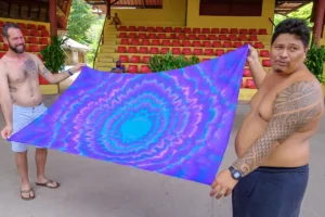 Deux homme tiennent un paréo coloré tendu entre eux après un atelier de confection de Paréo. Ils sont au milieu de la scène du Tiki Village ° Moorea