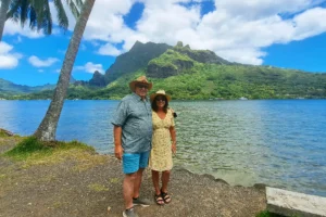 Couple posant au bord de la baie de Cook avec cocotiers et montagnes de Moorea en arrière-plan