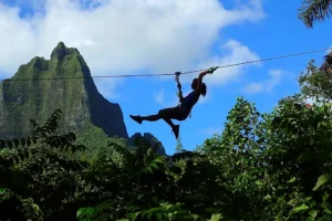 Participant lancé sur une tyrolienne au-dessus de la forêt tropicale du Tiki Parc avec montagne en arrière-plan