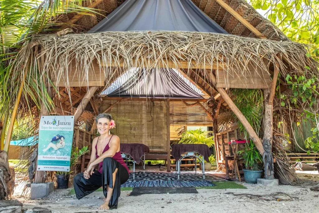 Une femme est accroupie devant un institut de massage à Moorea. Une affiche indique le nom MooJanzu