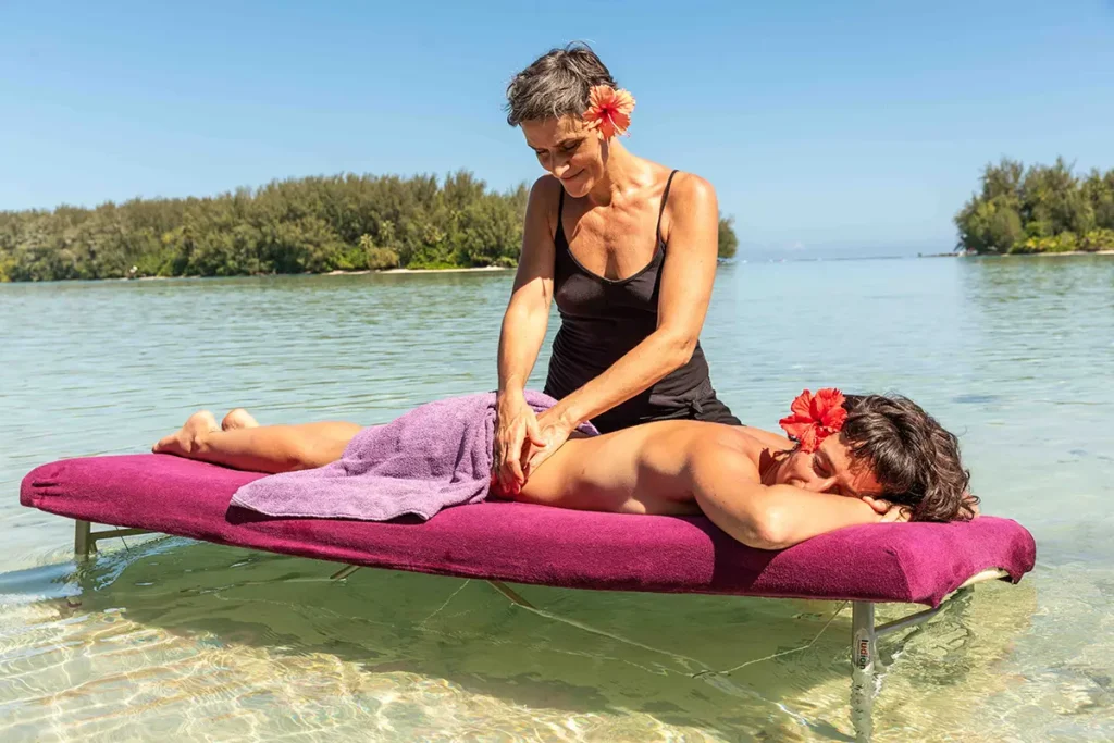 Une femme masse le dos d'une autre femme allongée sur une table de massage qui est installée dans le lagon de Moorea