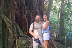 Couple standing by the roots of a large banyan tree on the guided 3 Pinus trail in Moorea