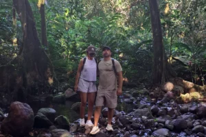 Couple marchant dans le lit rocheux d’une rivière sous les grands mape du Sentier des Ancêtres