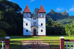 White facade and two red bell towers of Sainte-Famille Church in Haapiti with Moorea mountains