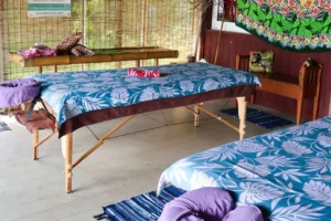 Tables de massage préparées avec paréos bleus et coussins violets dans un espace traditionnel à Moorea