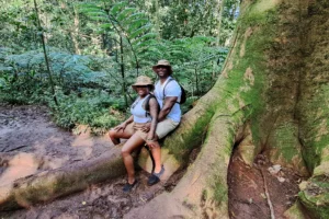 Couple sitting beside the large roots of a mape tree in Moorea forest during a guided hike
