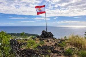 French Polynesian flag flying on the rocky summit of Mount Paaru Iti overlooking the ocean