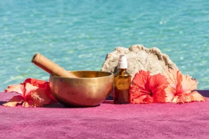 Bol chantant, huile de massage et fleurs d’hibiscus disposés face au lagon de Moorea