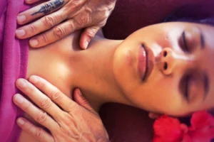 Gros plan sur les mains pratiquant un massage des épaules sur une femme détendue avec fleurs d’hibiscus