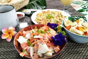 Vue d'ensemble d'une table de petit déjeuner dans un restaurant à Moorea. Des plats y sont présentés: poisson cru, salade de fruit, œufs brouillés et tasse de café.