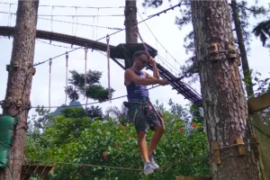 Participant franchissant un atelier d’équilibre suspendu entre les arbres au Tiki Parc à Moorea