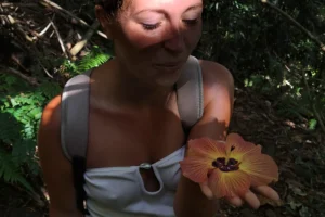 Woman holding an orange tropical flower in the forest during the 3 Pinus hike in Moorea