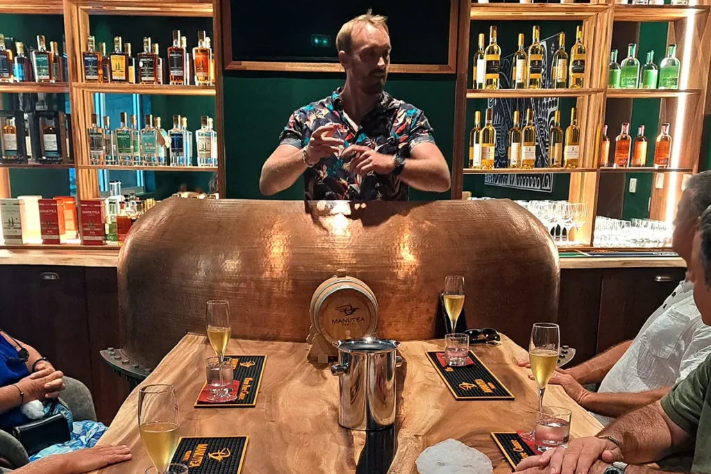 Un homme fait une prestation de dégustation privée de rhum et alcools dans la salle VIP de l'usine Rotui à Moorea. Il se tient derrière un bar en cuivre et une longue table en bois.