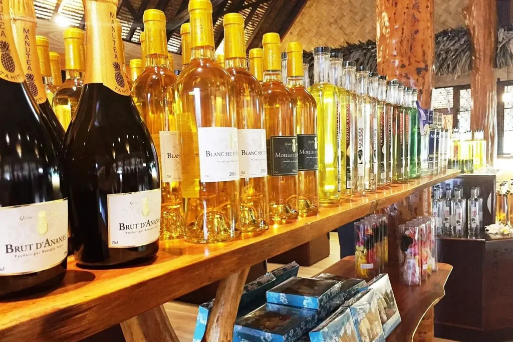 Des bouteilles de champagne brut d'ananas et de vin sont posées sur une étagère en bois du magasin d'usine de Rotui à Moorea