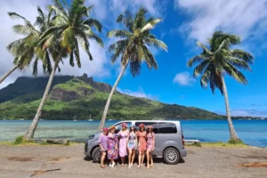 Six women posing beside the Moorea Private Tours vehicle under palm trees by Cook’s Bay