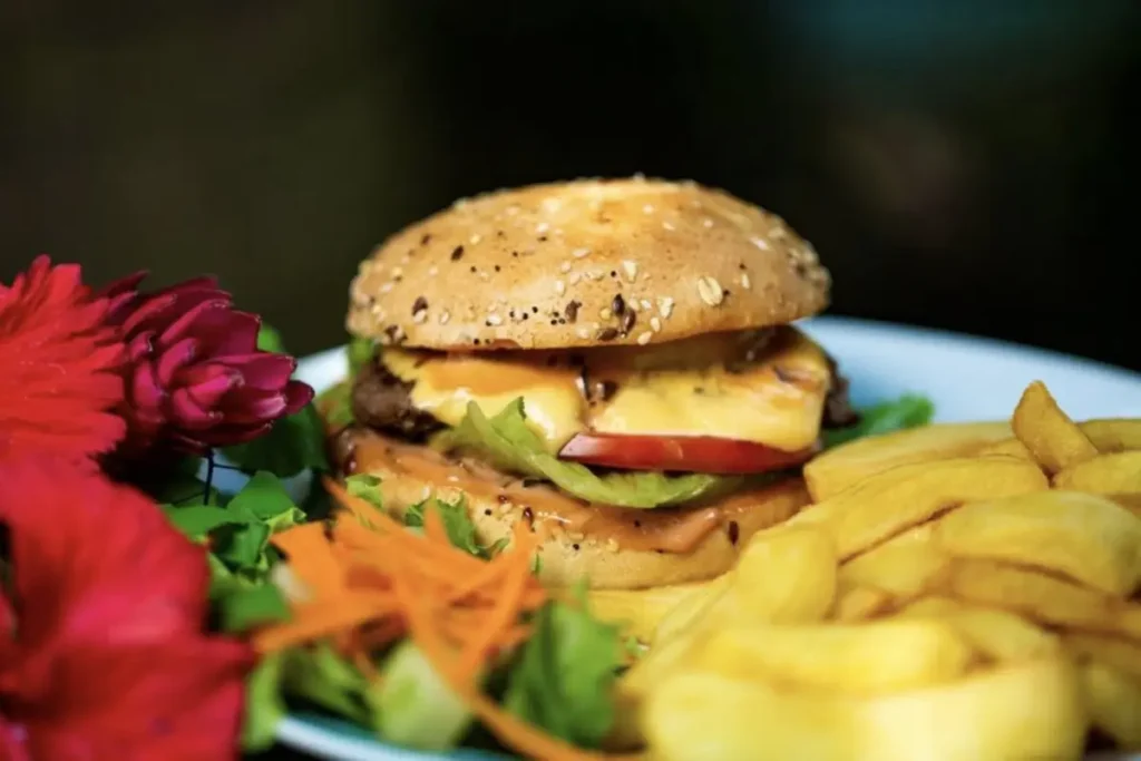 Gros plan sur un hamburger servi dans une assiette blanche avec des frites. Des fleurs rouges sont posées sur le coté gauche de l'assiette.