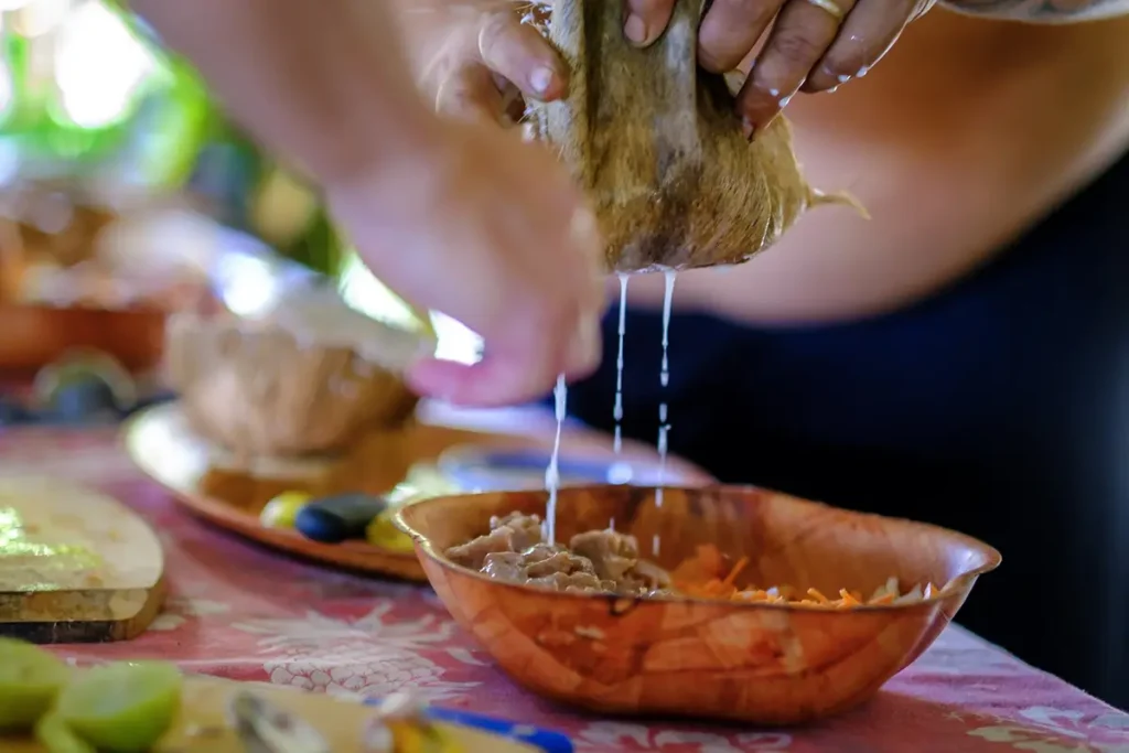Gros plan sur les main d'un homme versant du lait de coco frais sur un plat de poisson cru à le Tahitienne lors d'un atelier culinaire à Moorea
