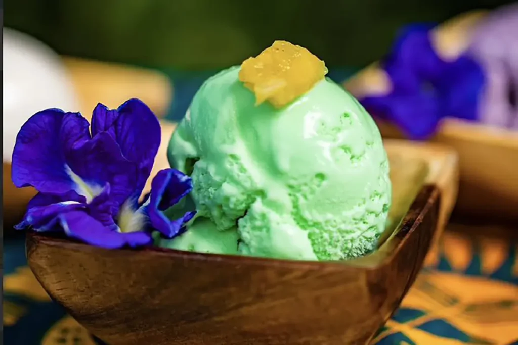 Une boule de crème glacée avec une fleur bleue violette posée dans un petit bol carré en bois