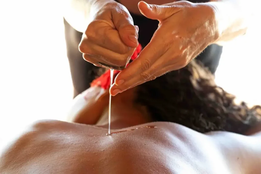 Une femme fait couler de l'huile de massage sur le dos d'une femme tahitienne allongée en vue de la préparation à un massage Tahitien