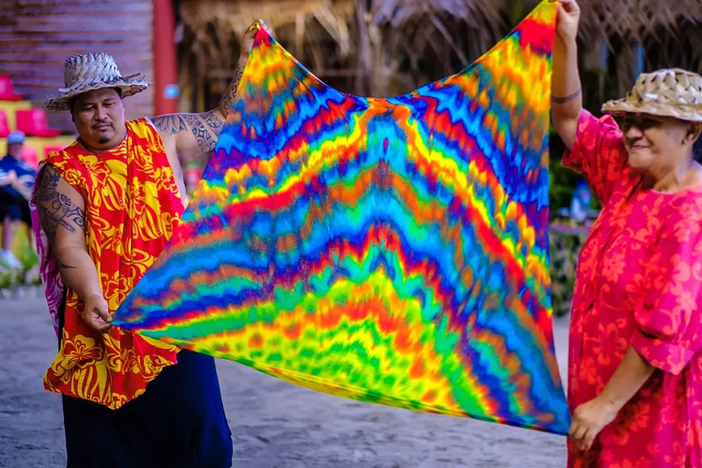 Un homme et une femme tahitiens tiennent tendu entre leur bras un pareo coloré