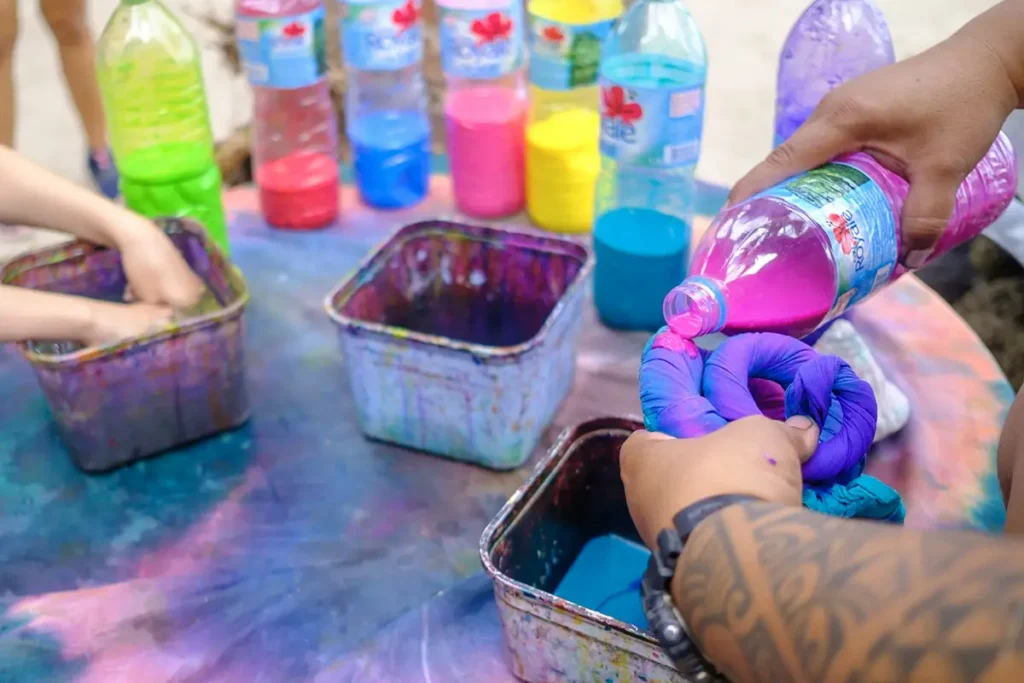 Vue rapprochée sur les mains d'un homme versant de la teinture de couleur rose sur un tissus de paréo