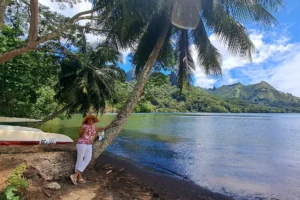 Woman beside a palm tree on a black-sand beach at Opunohu Bay with the mountains of Moorea