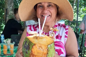 Femme souriante tenant une noix de coco fraîche avec une paille pendant une dégustation à Moorea