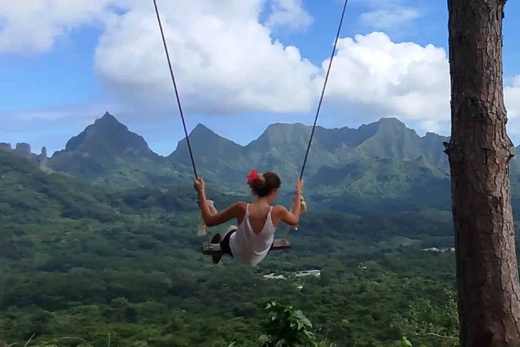 Une jeune femme fait de la balançoire, les pieds dans le vide au dessus de la vallée d'Opunohu à Moorea